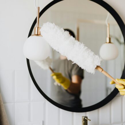 A person cleaning an elegant bathroom mirror with a fluffy duster and yellow gloves.