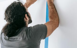 A man applying blue tape on a wall during a home renovation project, showcasing painting preparation.