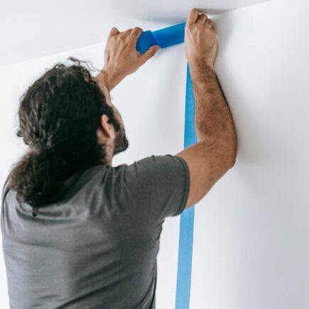 A man applying blue tape on a wall during a home renovation project, showcasing painting preparation.