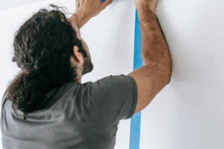 A man applying blue tape on a wall during a home renovation project, showcasing painting preparation.